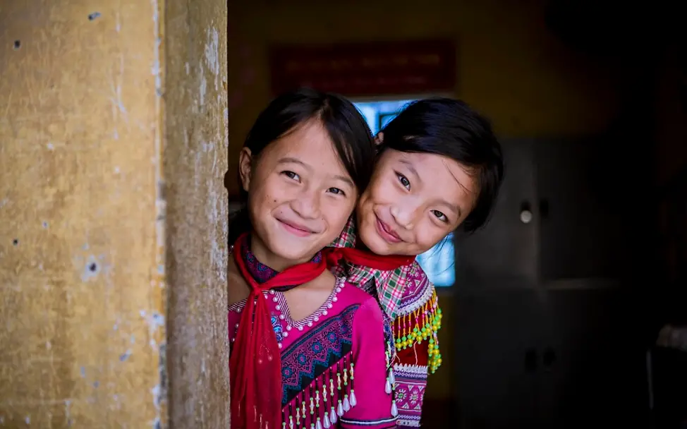 UNICEF wird 75 Jahre alt: Aktionen und Materialien | © UNICEF/Viet Hung Viertnam: Zwei Mädchen gucken hinter einer Mauer hervor und lächeln.