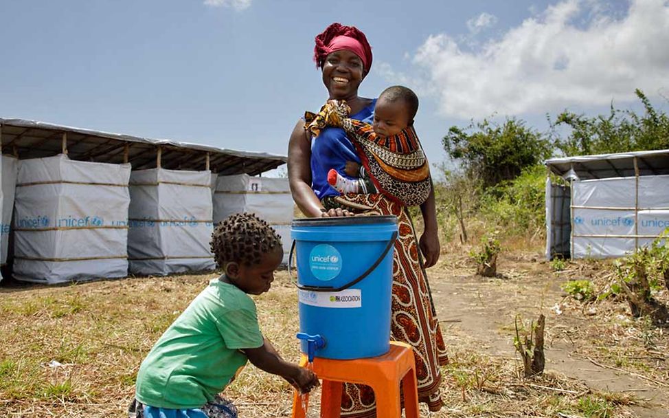 Nothilfe Mosambik: Sauberes Wasser ist elementar. Eine Mutter mit ihren Kindern an einer Händewaschstation.