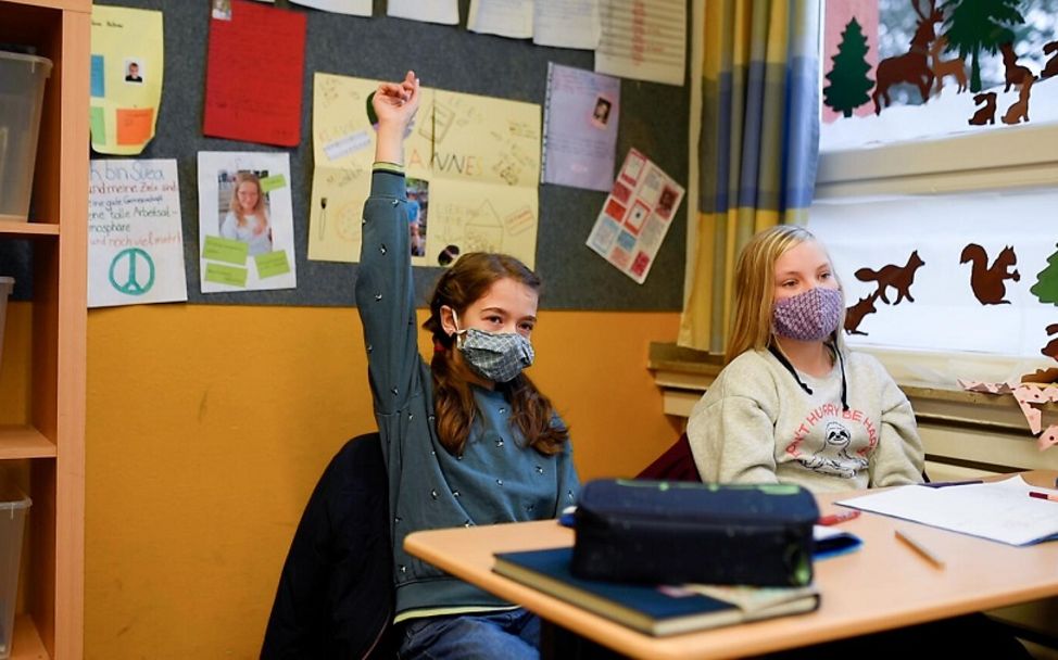 Corona: Schülerinnen sitzen mit Maske in der Schule und beteiligen sich am Unterricht.