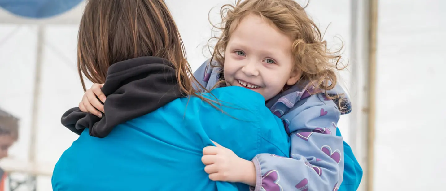 Eine UNICEF Helferin trägt ein lachendes Kind auf dem Arm in einer Anlaufstelle für Geflüchtete