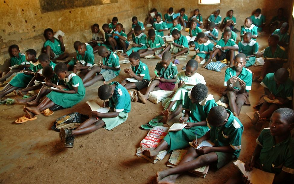 Schulen in Afrika: Kinder sitzen in ihren Schuluniformen auf dem Boden eines einfachen Schulgebäudes.