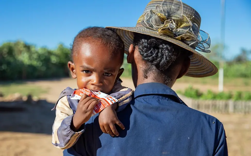 Gegen seine Mangelernährung erhält dieser Junge stärkende Erdnusspaste. | © UNICEF/Ralaivita Hungerkrise: Ein Junge in Madagaskar isst auf dem Arm seiner Mutter Erdnusspaste.
