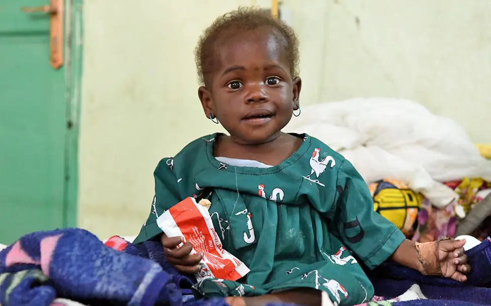 Ein Baby im Tschad ist dank der nahrhaften Erdnusspaste wieder zu Kräften gekommen. | © UNICEF/Dejongh Hungerkrise: Ein mangelernährtes Baby im Tschad hält eine Packung Erdnusspaste in der Hand.