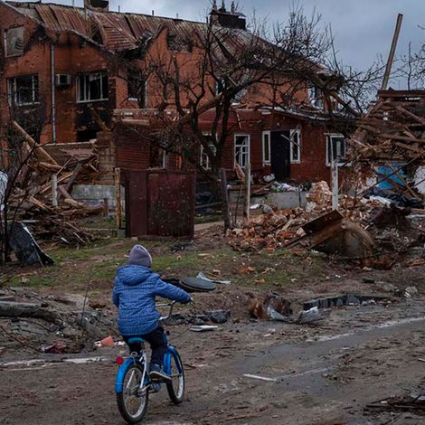 Ukraine-Krieg 100 Tage: Ein Kind in Tschernihiw fährt auf dem Fahrrad an zerstörten Häusern vorbei.