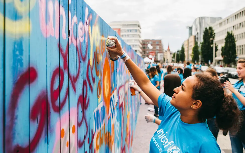 Sprayen für eine gerechtere Welt. | © UNICEF Mädchen in unicef Shirt sprayt "unicef" auf eine Wand