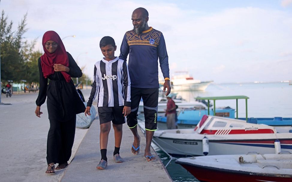 Malediven: Fathimath spaziert mit ihrem Vater und ihrem Bruder am Hafen entlang, neben ein paar kleinen Booten.