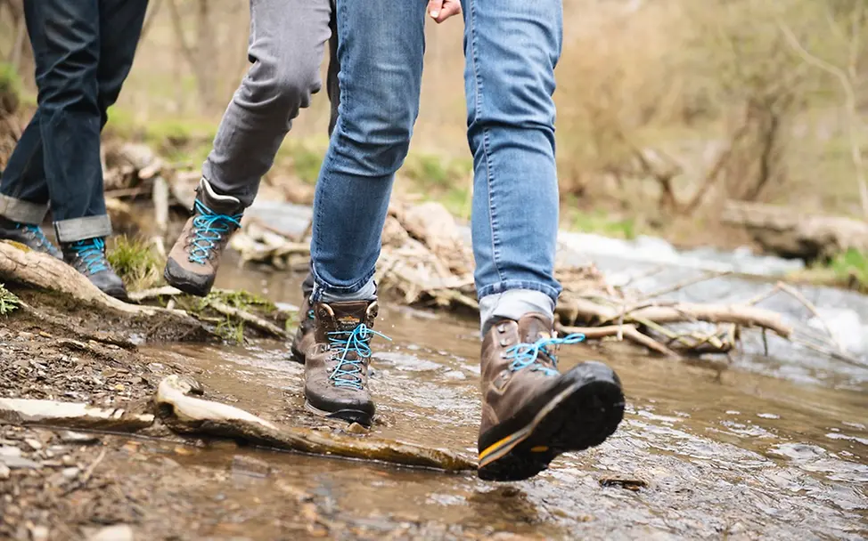 Wandern gegen die Wasserkrise I UNICEF/Etges Man sieht Beine von Menschen, die mit Wanderschuen durch einen Bach gehen.