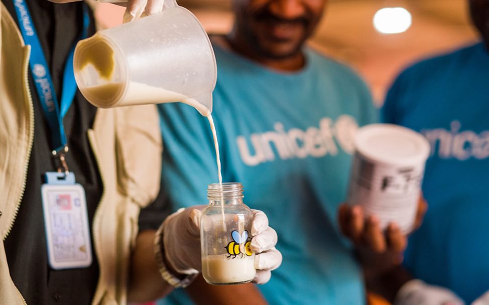 Nothilfe im Sudan-Krieg: Ein UNICEF-Helfer bereitet eine Flasche mit Spezialmilch für ein mangelernährtes Kleinkind vor. 