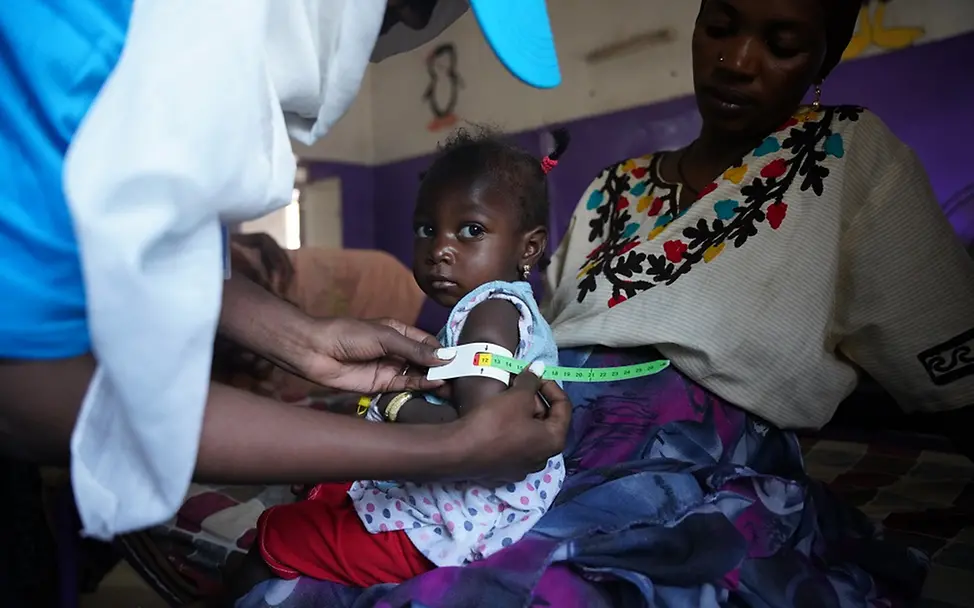 UNICEF: Jede Stunde kommt es zu schweren Kinderrechtsverletzungen im Sudan | UNICEF/Awad Sudan: Einem kleinen Mädchen, das auf dem Schoß der Mutter sitzt, wird ein Messband um den Arm gelegt.