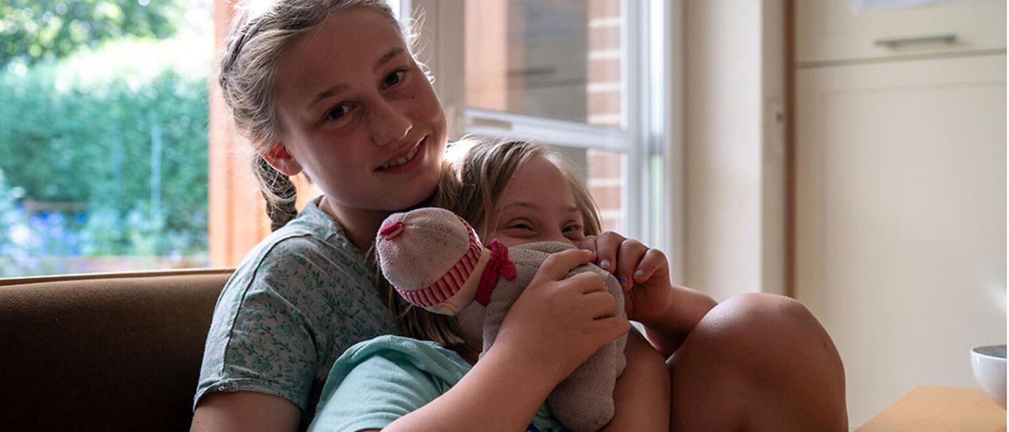 Nina (13) und Helen (10) sitzen in der Küche und kuscheln.