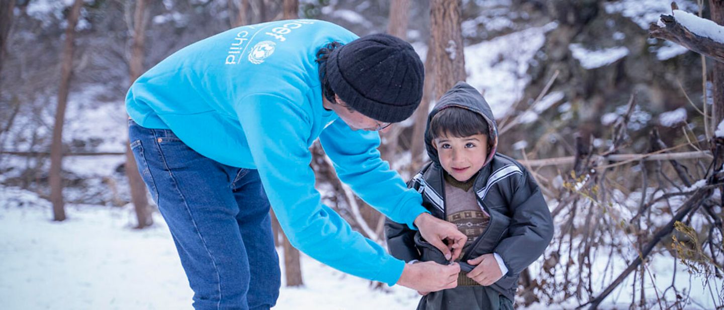 UNICEF-Winterhilfe: Winter in Pakistan: Ein UNICEF-Helfer zieht einem Jungen im Schnee eine Winterjacke an