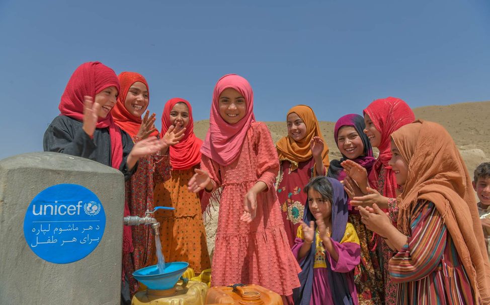 Mädchen in Afghanistan füllen an einem Brunnen Wasser in Kanister. 