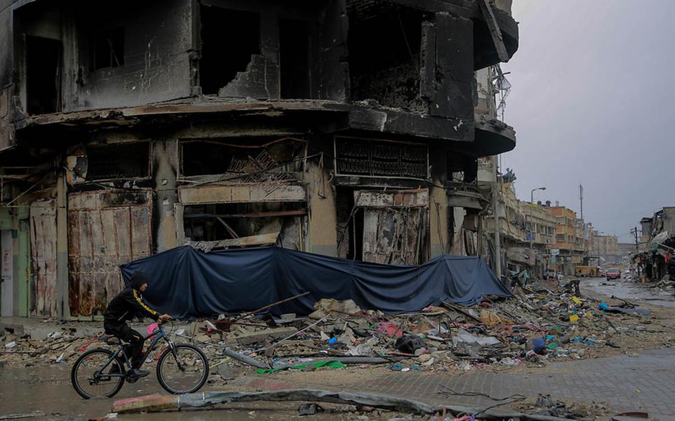 Gaza Kinder: Ein Junge fährt auf seinem Fahrrad an einem völlig zerstörten Wohnhaus vorbei