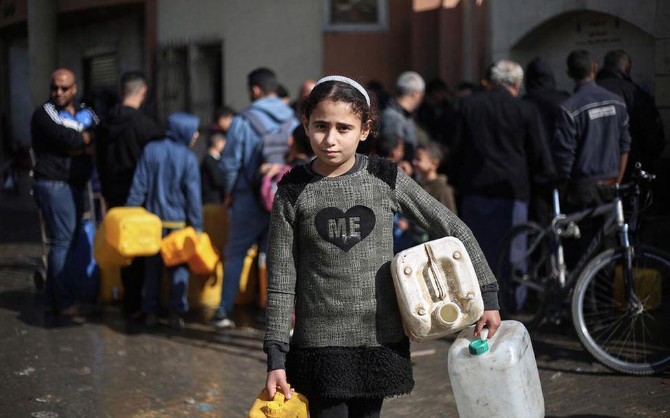 Kinder in Gaza: Ein Mädchen trägt Kanister unterm Arm, die sie mit Trinkwasser füllen möchte