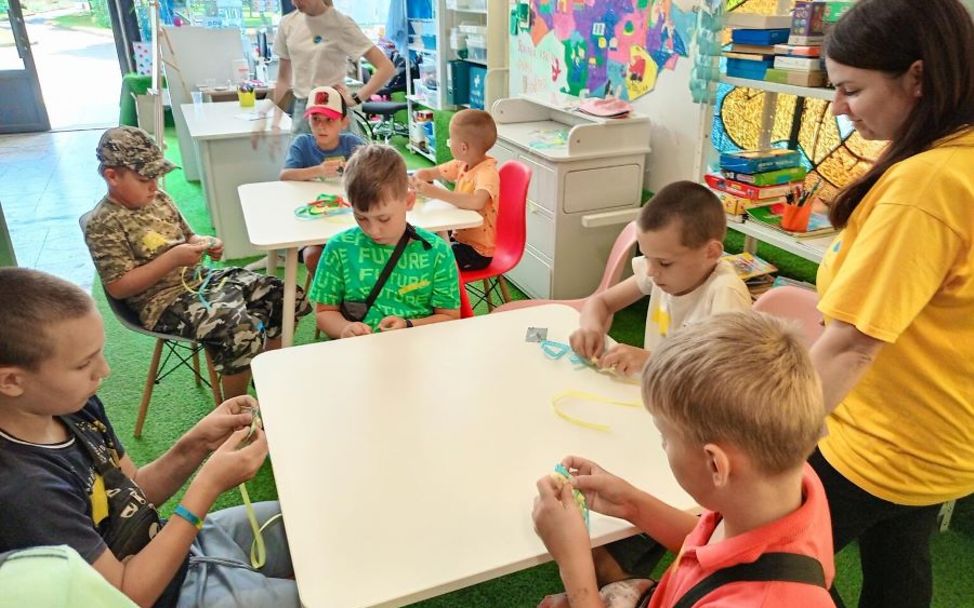 Jahrestag Ukraine-Krieg: Kinder sitzen an einem Tisch und basteln Armbänder.