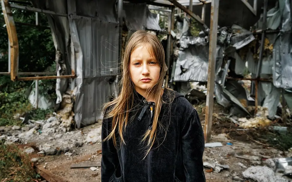 Zwei Jahre Krieg in der Ukraine: Die Lage der Kinder | UNICEF/Hrom Ukraine: Die zehnjährige Arina steht vor einem zerstörten Gebäude in der Region Charkiw.