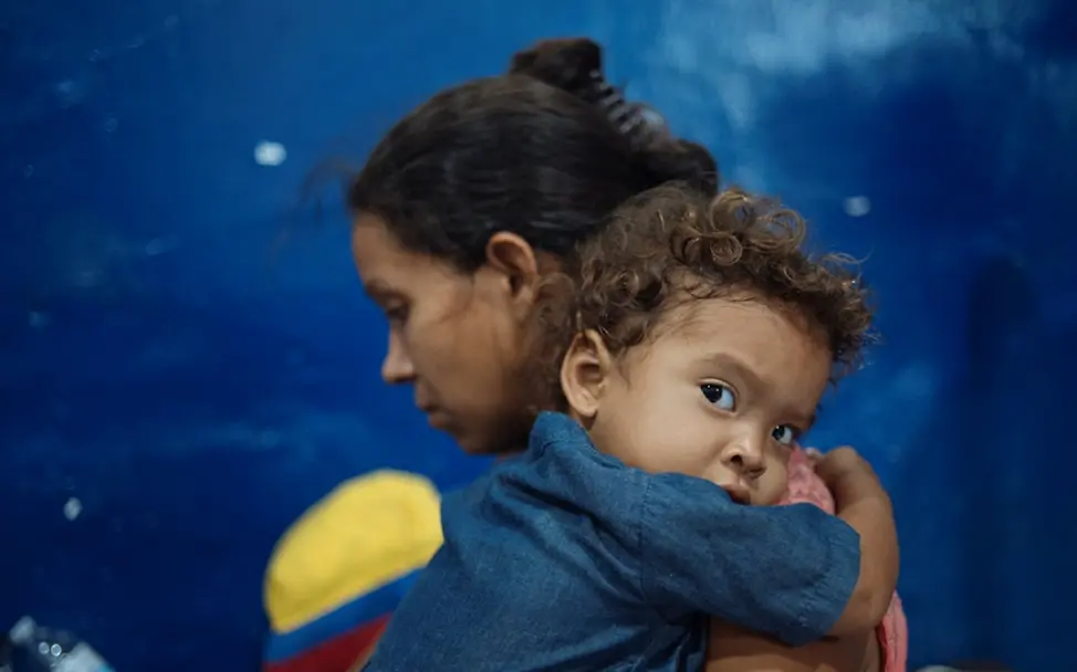Maikel hält ihre Mutter Leidy Characo in der Raststätte in Kolumbien für Wanderer, die ihre Reise von Venezuela aus zu Fuß fortsetzen | © UNICEF/UN0304104/Arcos Weltflüchtlingstag: Maikel hält ihre Mutter Leidy Characo in der Raststätte in Kolumbien, wo sie ihre Reise zu Fuß fortsetzen