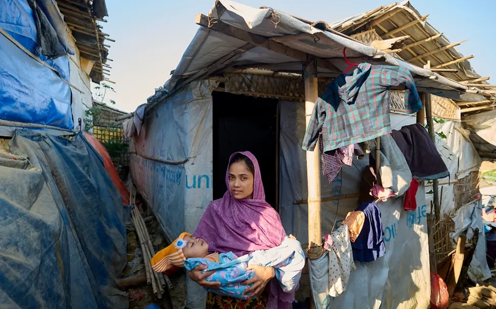 Ein Porträt einer jungen Mutter mit ihrem Baby vor ihrer Hütte im Rohingya-Flüchtlingslager | © UNICEF/UN0599873/Map Weltflüchtlingstag: Ein Porträt einer jungen Mutter mit ihrem Baby vor ihrer Hütte im Rohingya-Flüchtlingslager