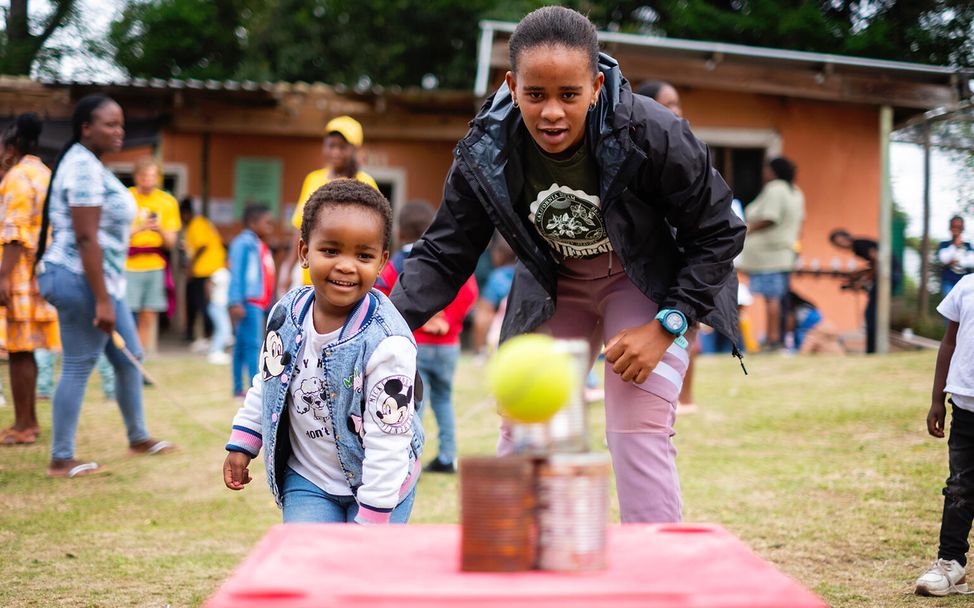 In Südafrika spielen Eltern und Kinder Dosenwerfen.