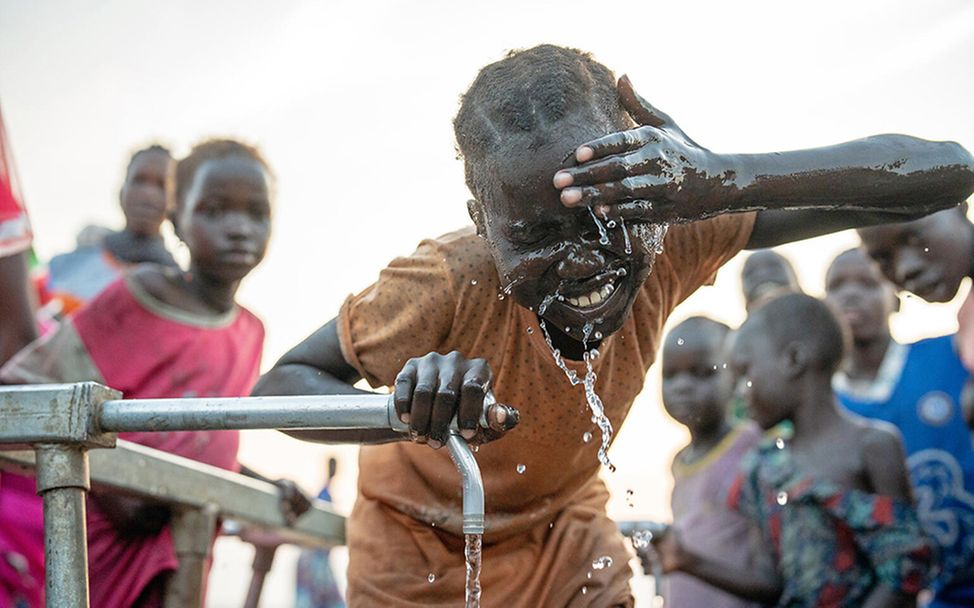 Südsudan: Ein Mädchen kühlt ihren Kopf an einer Wasserstelle.