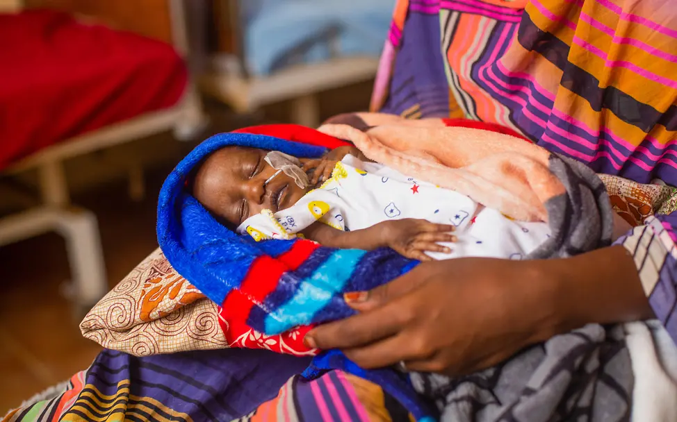 Mangelernährung ist eines der größten Probleme im Sudan | © UNICEF/UNI626271/Isamaldeen Ein Baby mit einer Sonde in der Nase auf dem Schoß seiner Mutter