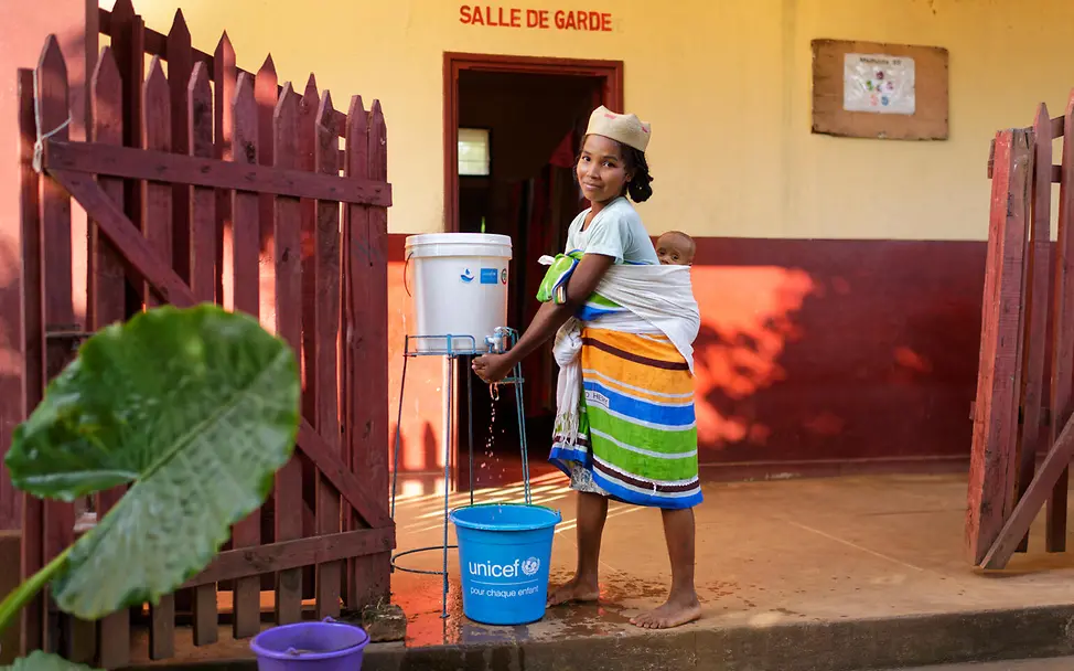 Hygiene für Schwangere und Kinder | © UNICEF/UNI400590/Ramasomanana Eine Frau mit ihrem Baby auf dem Rücken wäscht sich die Hände