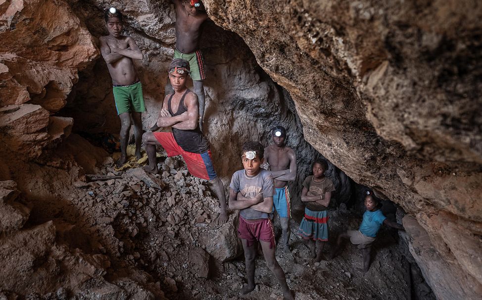 Sieben Kinder stehen in einer Höhle die zu einer Mine führt in der sie arbeiten müssen