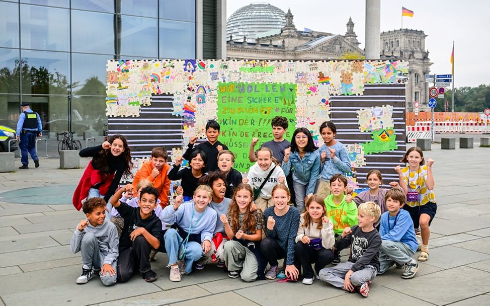 Kinder stehen vor einer Wand, die geschmückt ist mit ihren selbst gestalteten Puzzleteilen.