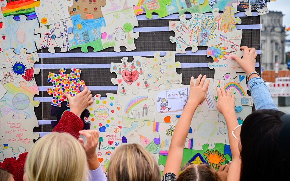 Kinder befestigen ihre selbst gestalteten Puzzleteile an einer Wand.