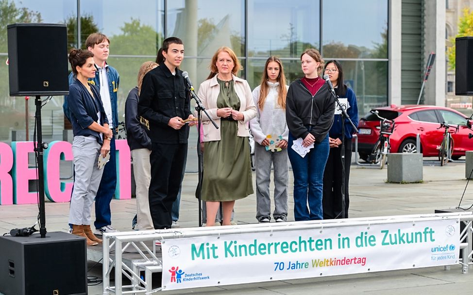 Kinder stehen auf einer Tribüne und halten eine Rede.