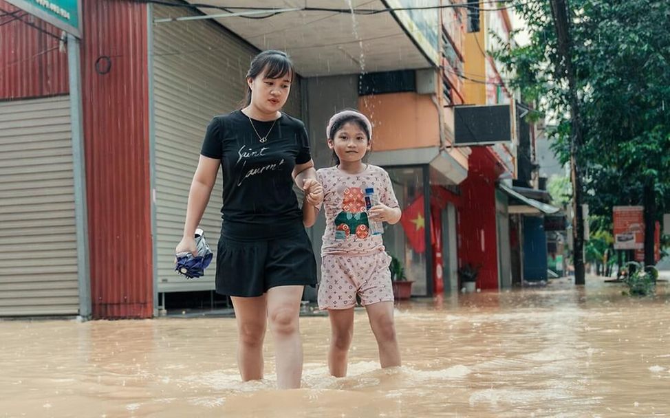 Taifun Yagi in Vietnam: Eine Frau und ein Mädchen waten durch Hochwasser