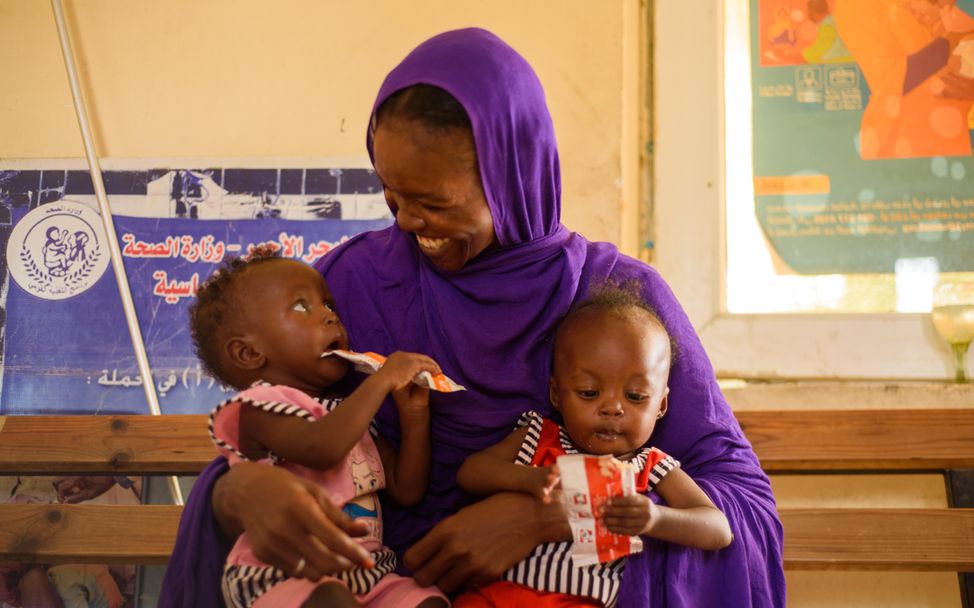 A mother is holding her twin daughters in her arm