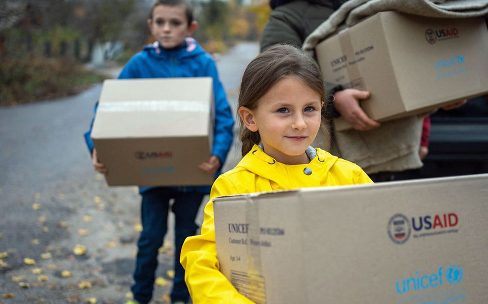 Kinder im Ukraine-Krieg: Ein Mädchen hat einen Karton mit wärmender Winterkleidung bekommen. 