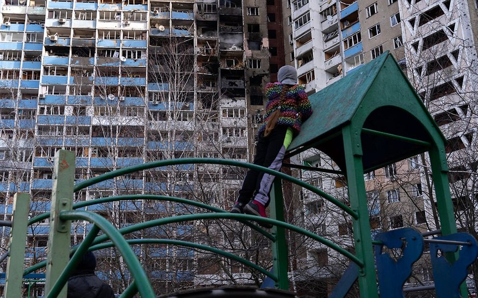 Ein Mädchen auf einem Spielplatz vor einem beschädtigten Gebäude in Kiew.