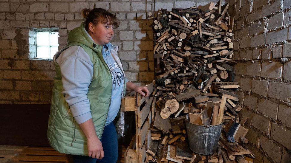 Ukraine Winter Hilfe: Eine Mutter in der Ukraine steht vor einem Stapel Brennholz für den Winter 