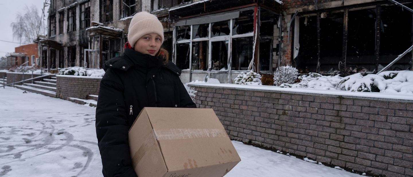 Sofia (12) trägt eine Kiste mit Winterkleidung, die sie bei der UNICEF-Winterkleidungsausgabe erhalten hat.