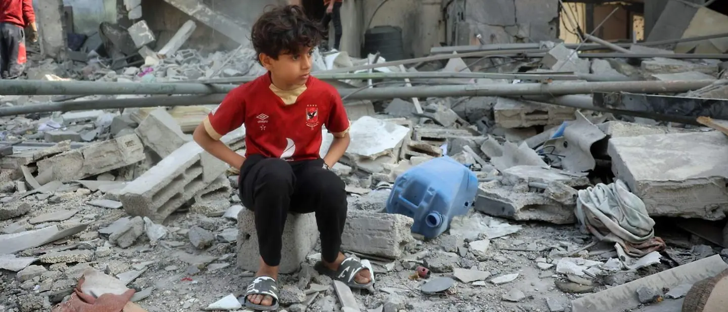 Gaza spenden: Ein Junge sitzt nach Luftangriffen in den Trümmern seines Zuhauses