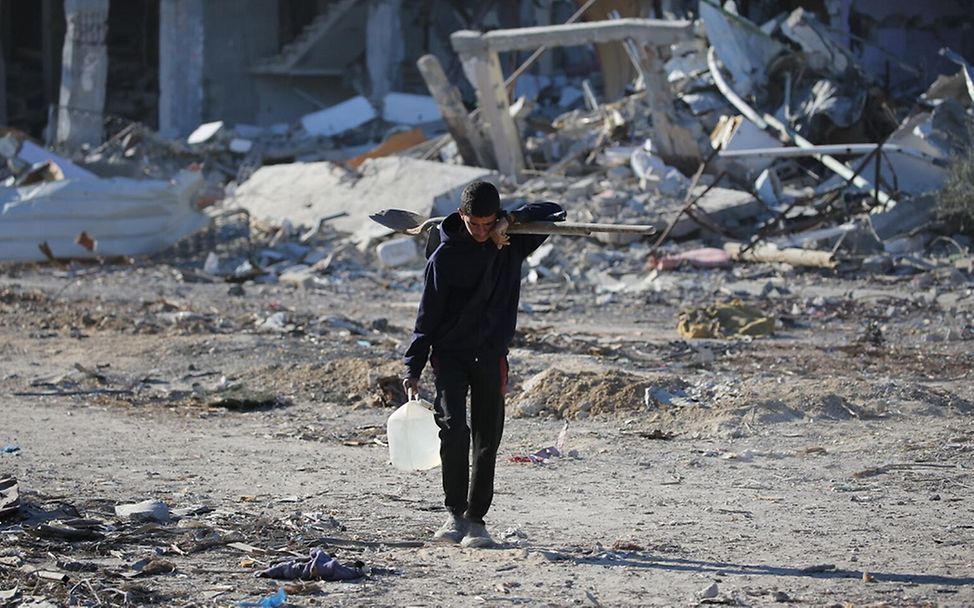 Ein Junge trägt einen Wasserkanister zwischen den Trümmern der Häuser in Rafah im Gazastreifen