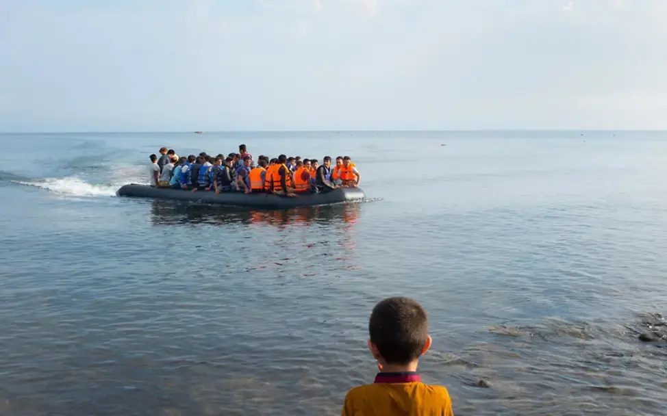 Flüchtlinge auf einem Schlauchboot in Ufernähe, ein Kind wartet auf die Ankunft Flüchtlinge auf einem Schlauchboot in Ufernähe, ein Kind wartet auf die Ankunft