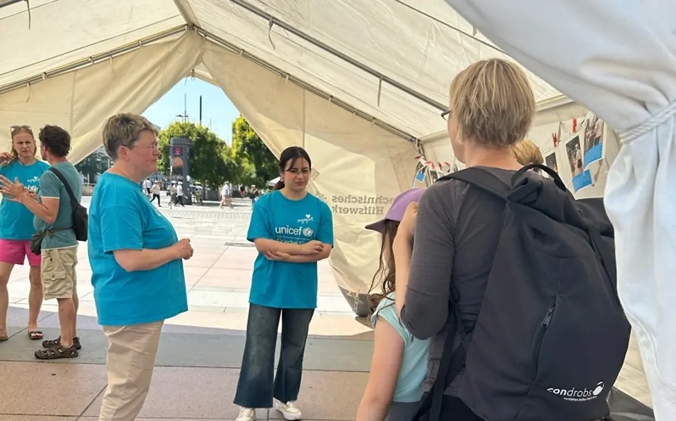 In einem großen weißen Zelt stehen und sitzen Interessierte und nehmen an der Aktion zum Weltflüchtlingstag teil