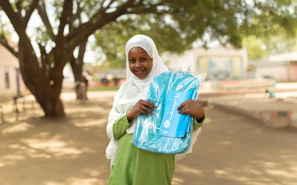 Spenden Sudan Nothilfe: Ein aus Khartum geflüchtetes Mädchen hält ihren UNICEF-Schulrucksack hoch