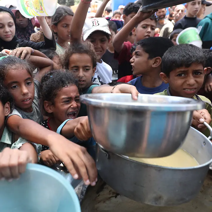 Gaza spenden: Kinder an einer Essensausgabe im Gazastreifen versuchen verzweifelt Nahrung in ihre Schüsseln zu bekommen. 