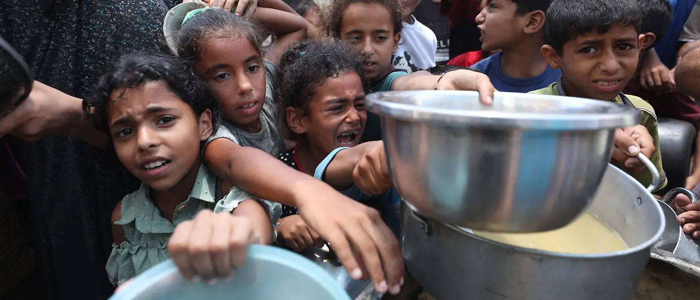 Gaza spenden: Kinder an einer Essensausgabe im Gazastreifen versuchen verzweifelt Nahrung in ihre Schüsseln zu bekommen. 