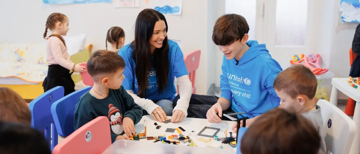 A mother and her teenage son sitting in a colourful room playing with children_