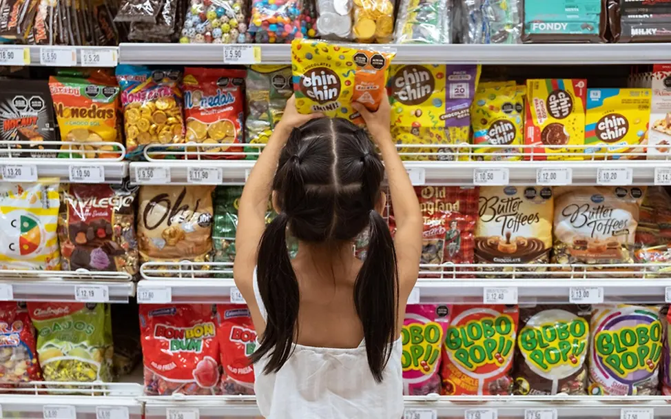 Micaella (8) greift im Supermarkt zu den Süßigkeiten. | © UNICEF/Goupil - Highway Child Kinder Ernährung: Micaella (8) greift im Supermarkt zu den Süßigkeiten.