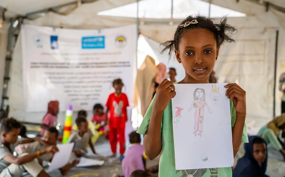 Sudan Krieg: Ein geflüchtetes Mädchen hat in einem Spielzelt von UNICEF ein Bild gemalt und zeigt es stolz. 