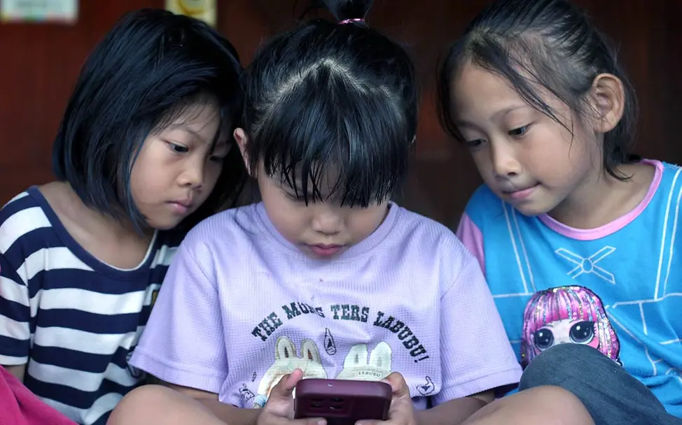 Digitale Gewohnheiten: Drei Mädchen in Malaysia schauen zusammen auf ein Smartphone. 