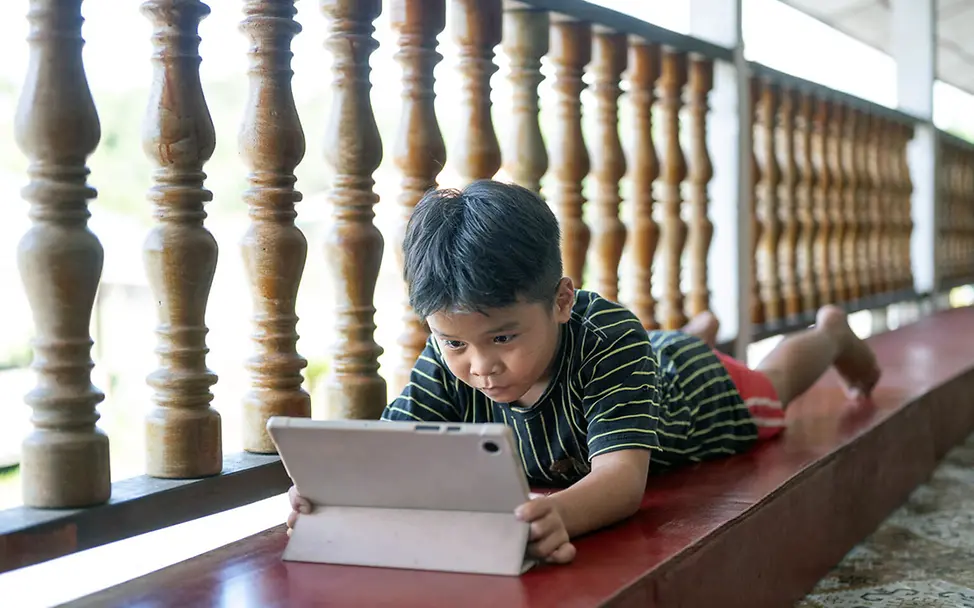 Digitale Gewohnheiten: Ein Junge in Malaysia liegt auf dem Bauch und schaut auf ein Tablet.