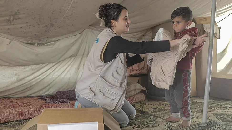 Gaza: UNICEF Helferin überreicht Kind Winterkleidung.