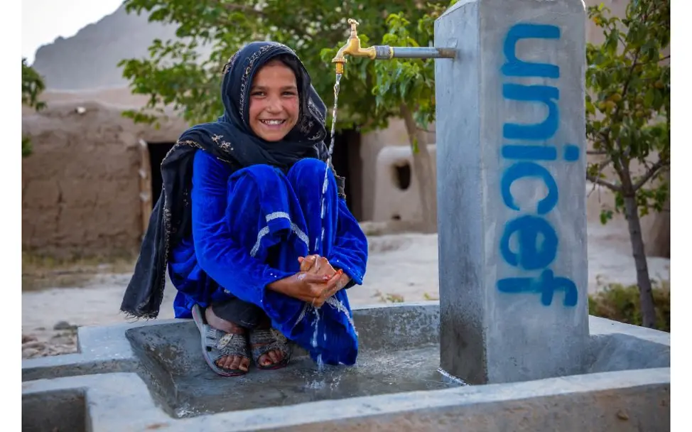 © UNICEF/Meerzad  Afghanistan: Mädchen sitzt an Brunnen.